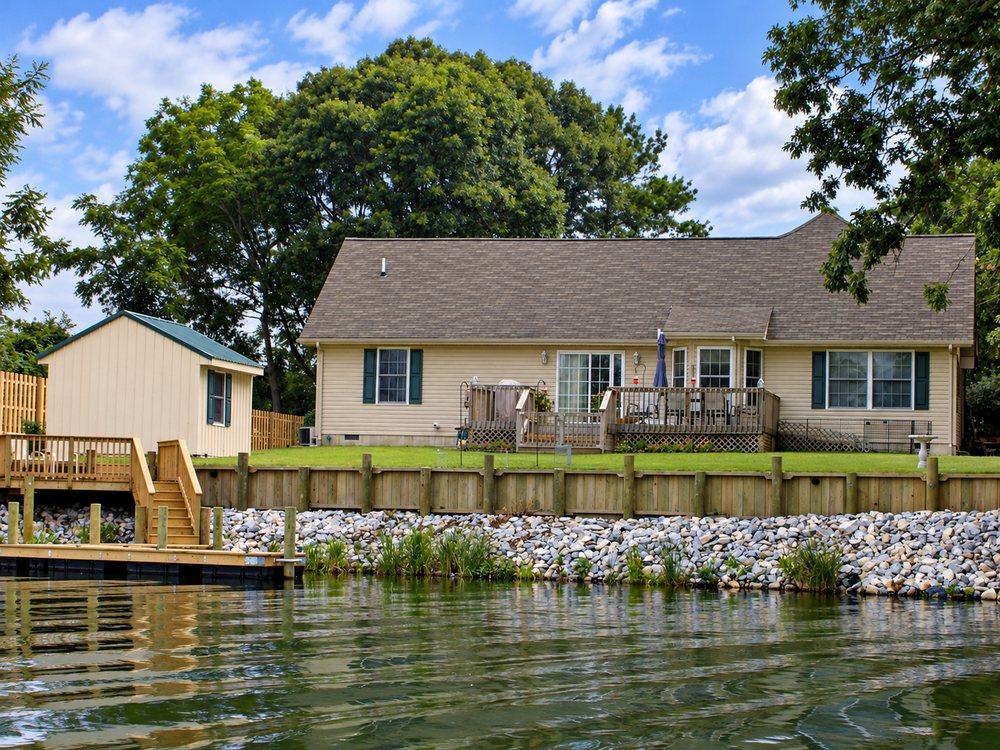 A finished timber bulkhead with rip-rap at its toe and a pier with access steps in front of a waterfront home.